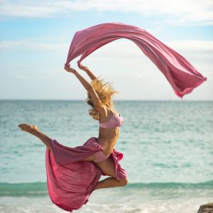 Concept of freedom and happiness. Happy woman on the beach jumping with flying pink silk.